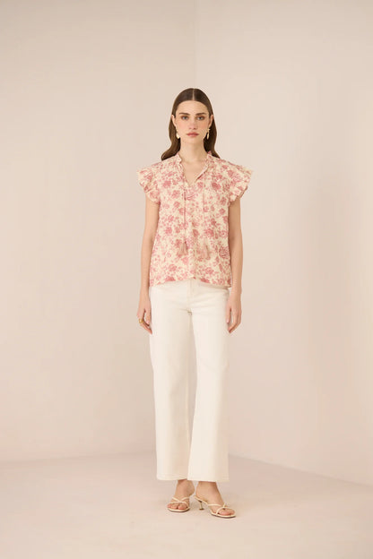 Model wearing the Madison Blouse in a soft floral print with white trousers, shown from the front.