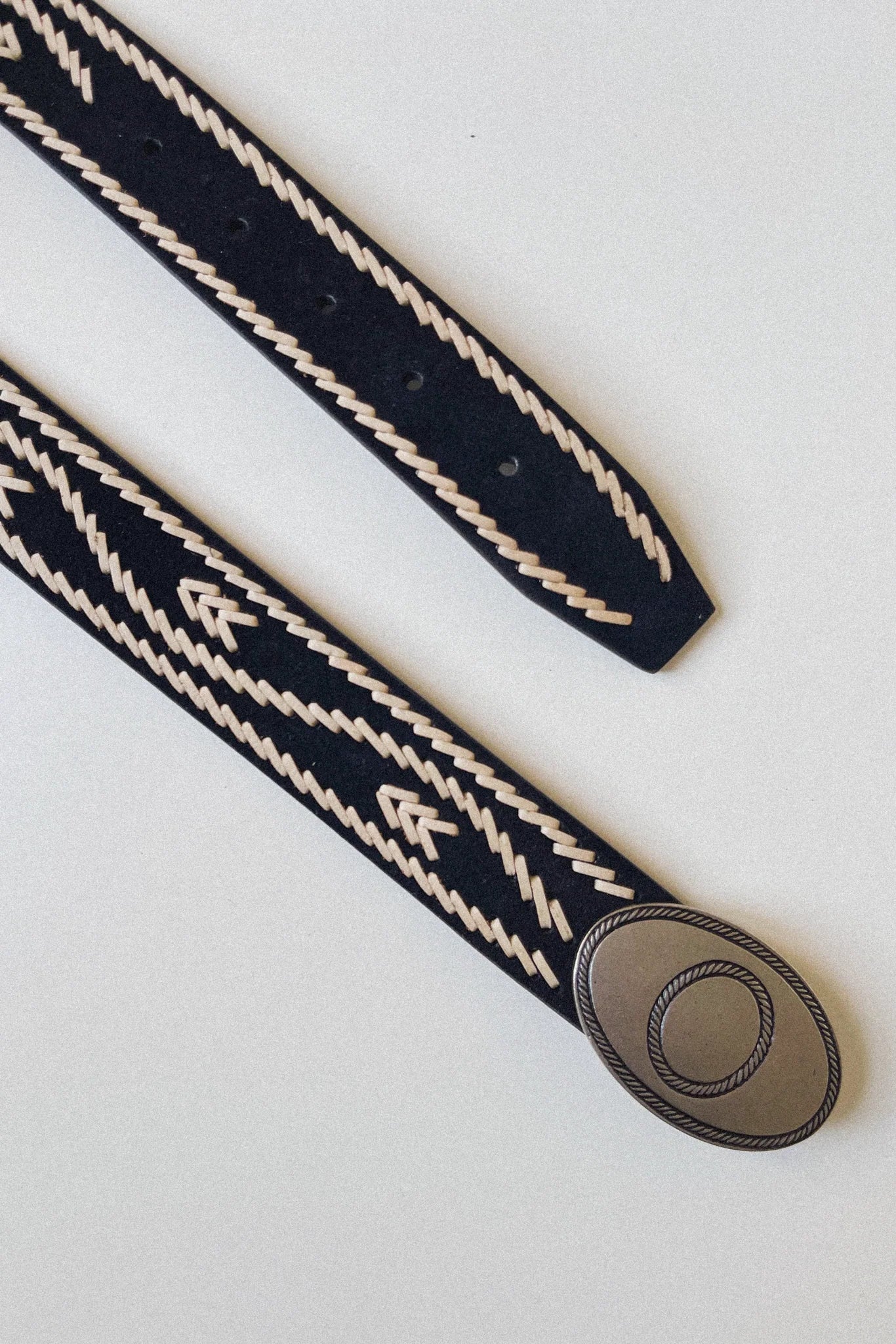 Full view of the Malambo Belt laid flat, showing the black woven strap, cream stitched detailing, adjustable holes, and oval buckle.