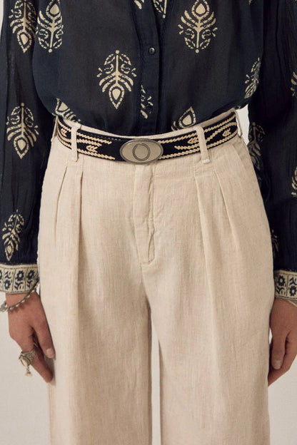 Malambo Belt styled around the waist with cream trousers and a black printed shirt, showing the black woven strap and oval gaucho-style buckle.