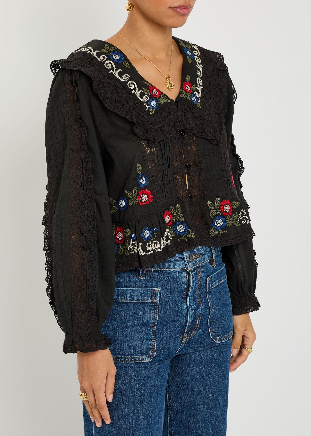 Angled view of the black Maribelle embroidered blouse with lace detailing, long sleeves, and colorful floral embroidery along the neckline and hem.