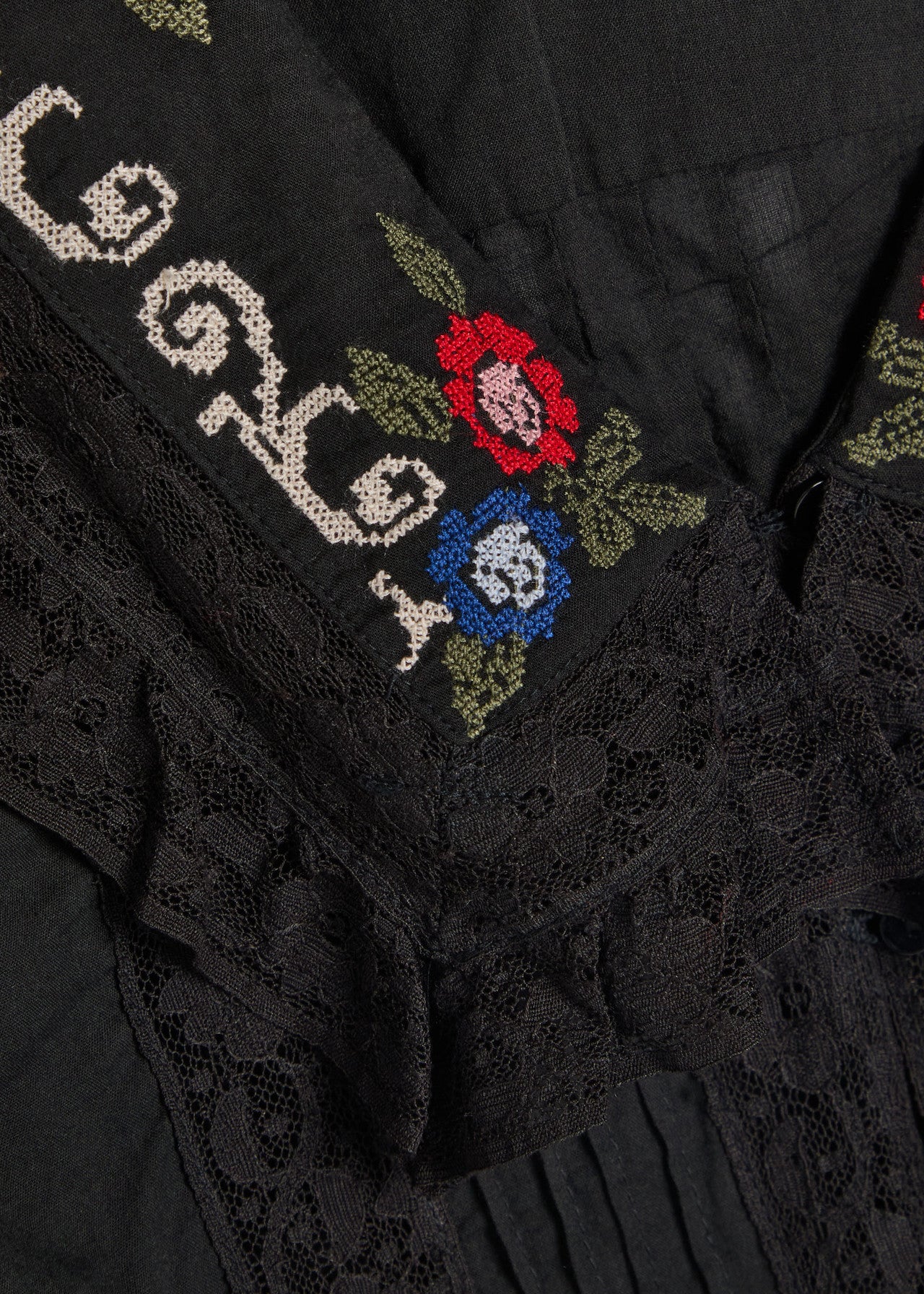 Close-up detail of the Maribelle Top showing intricate floral cross-stitch embroidery and delicate black lace trim on the neckline.