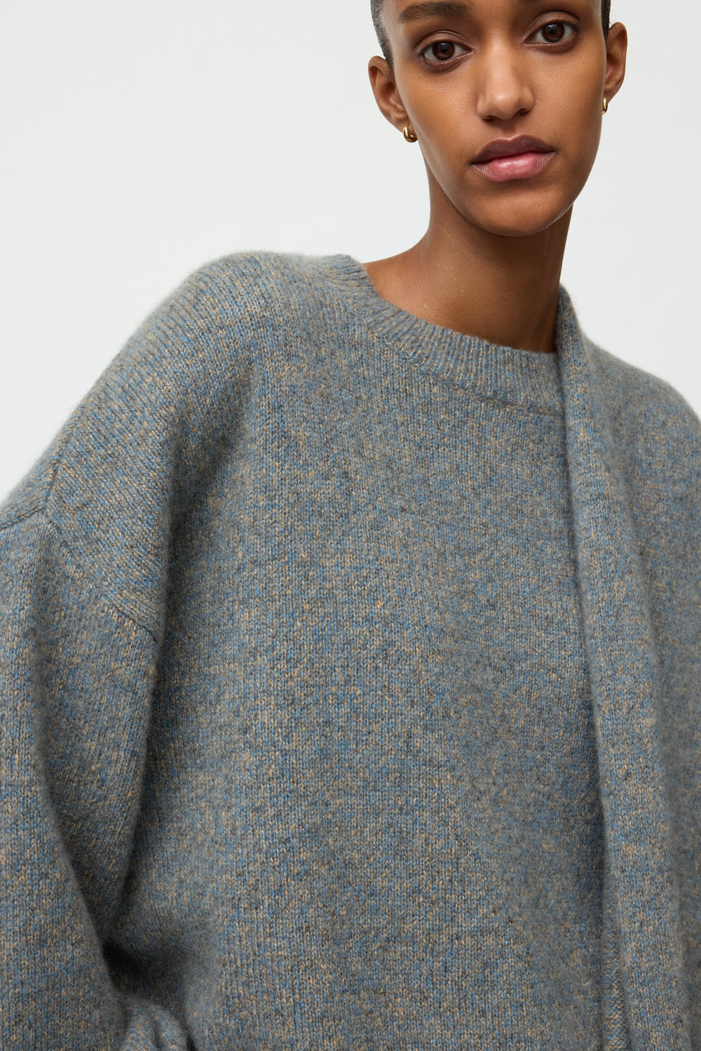 Close-up of the blue-grey marled crewneck showing its crew neckline, relaxed sleeve, and softly textured knit.