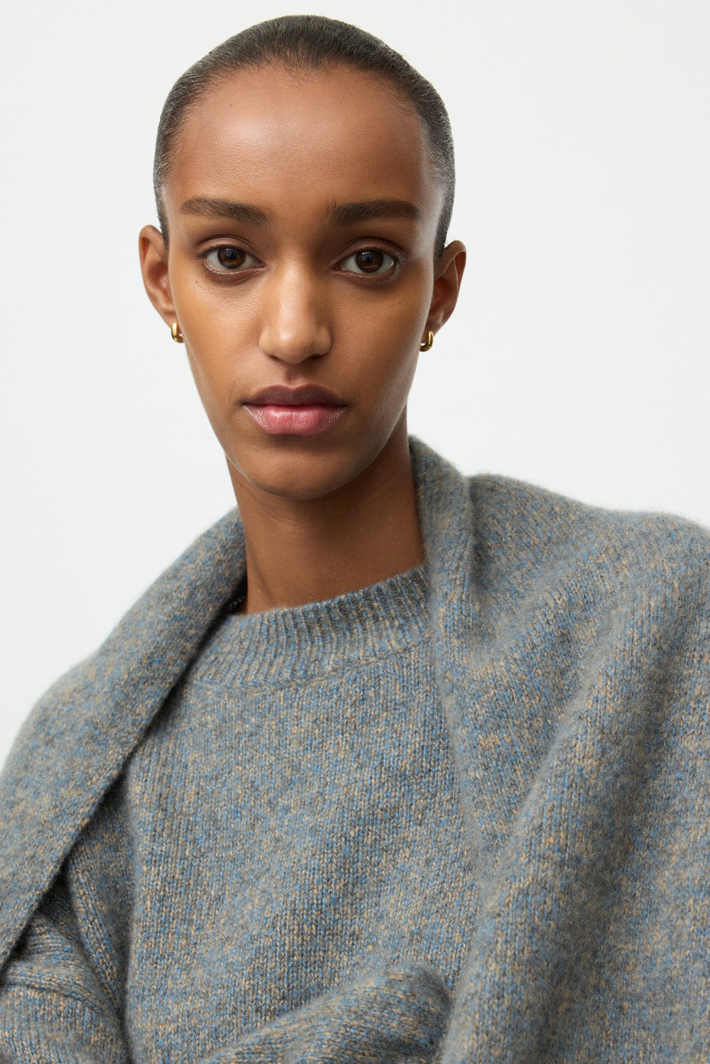 Close-up of the model wearing the blue-grey marled crewneck with a coordinating knit draped over the shoulders.