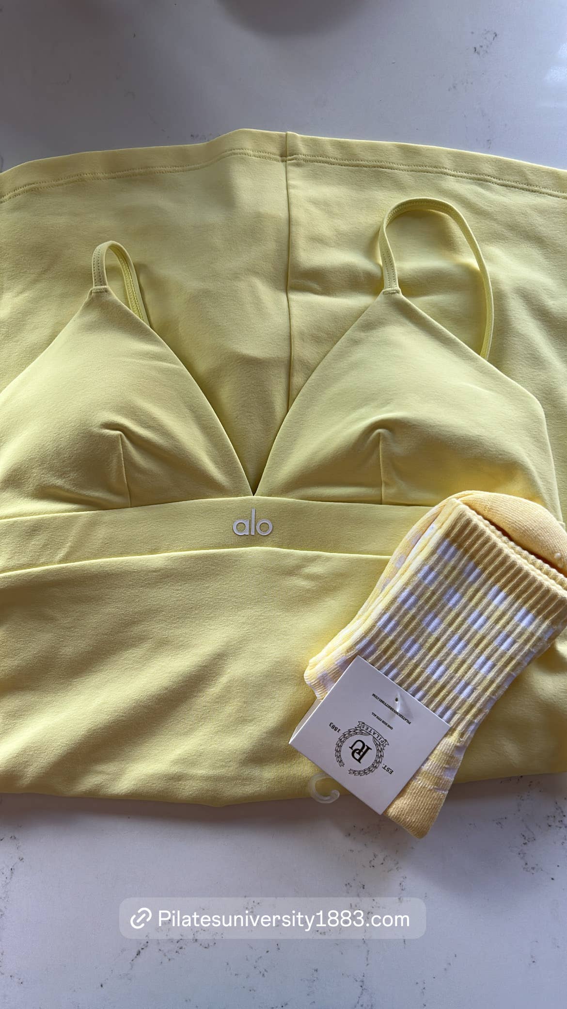 Yellow and white gingham grip socks displayed alongside coordinating pastel yellow activewear, featuring a ribbed cuff and non-slip silicone grips for Pilates, Barre, and studio workouts.