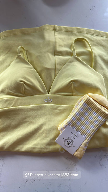 Yellow and white gingham grip socks displayed alongside coordinating pastel yellow activewear, featuring a ribbed cuff and non-slip silicone grips for Pilates, Barre, and studio workouts.