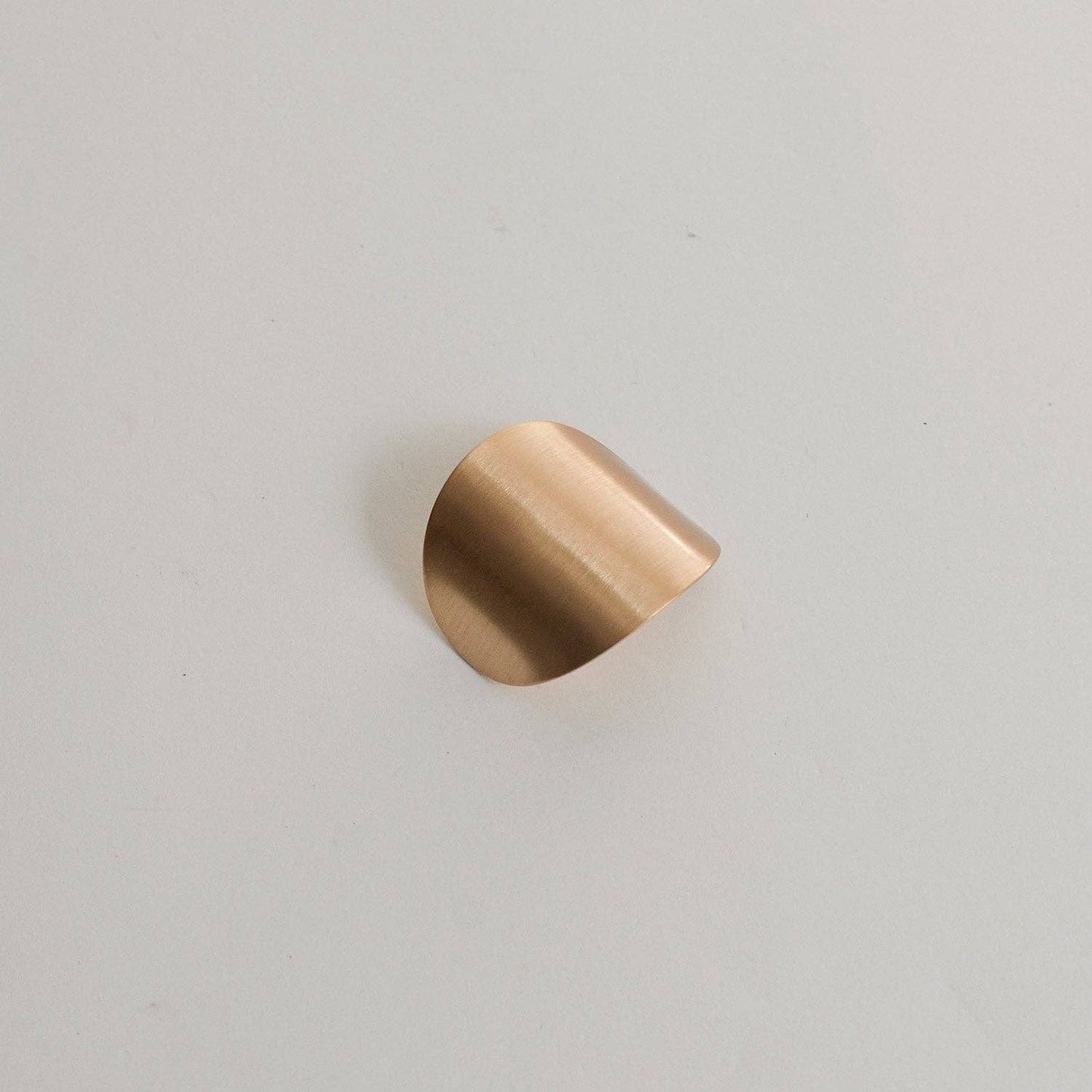 Profile view of the brushed gold oval metal cuff highlighting its softly curved shape.