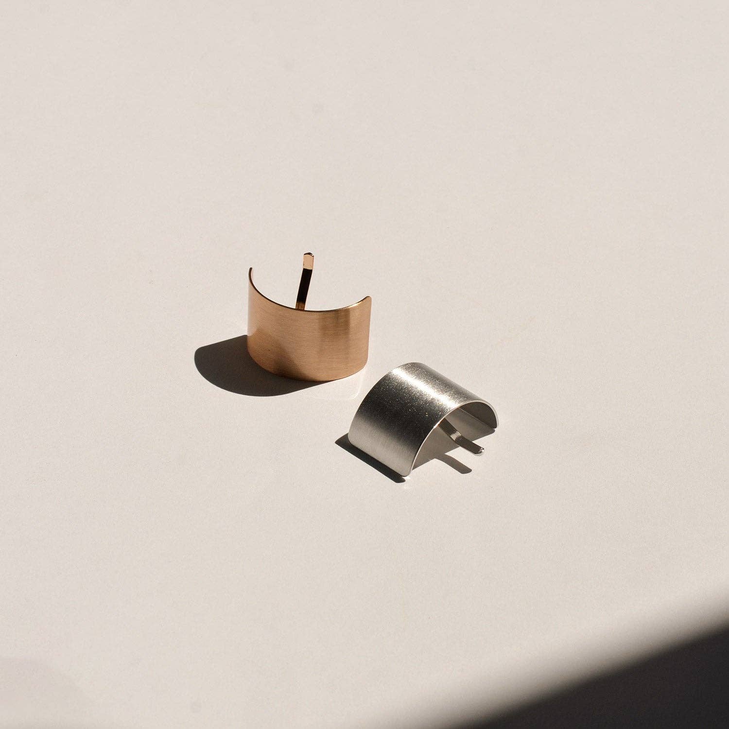 Silver and gold rectangular metal ponytail cuff sticks arranged together on a neutral surface.
