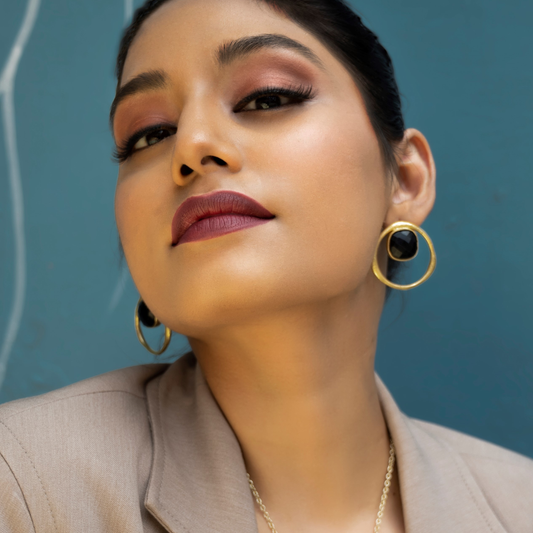 Close-up of a model wearing black onyx stud earrings with gold-plated circular frames.