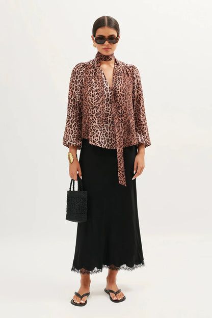 Model wearing the Moss leopard print silk blouse with a scarf neckline, black satin skirt, and sandals front view