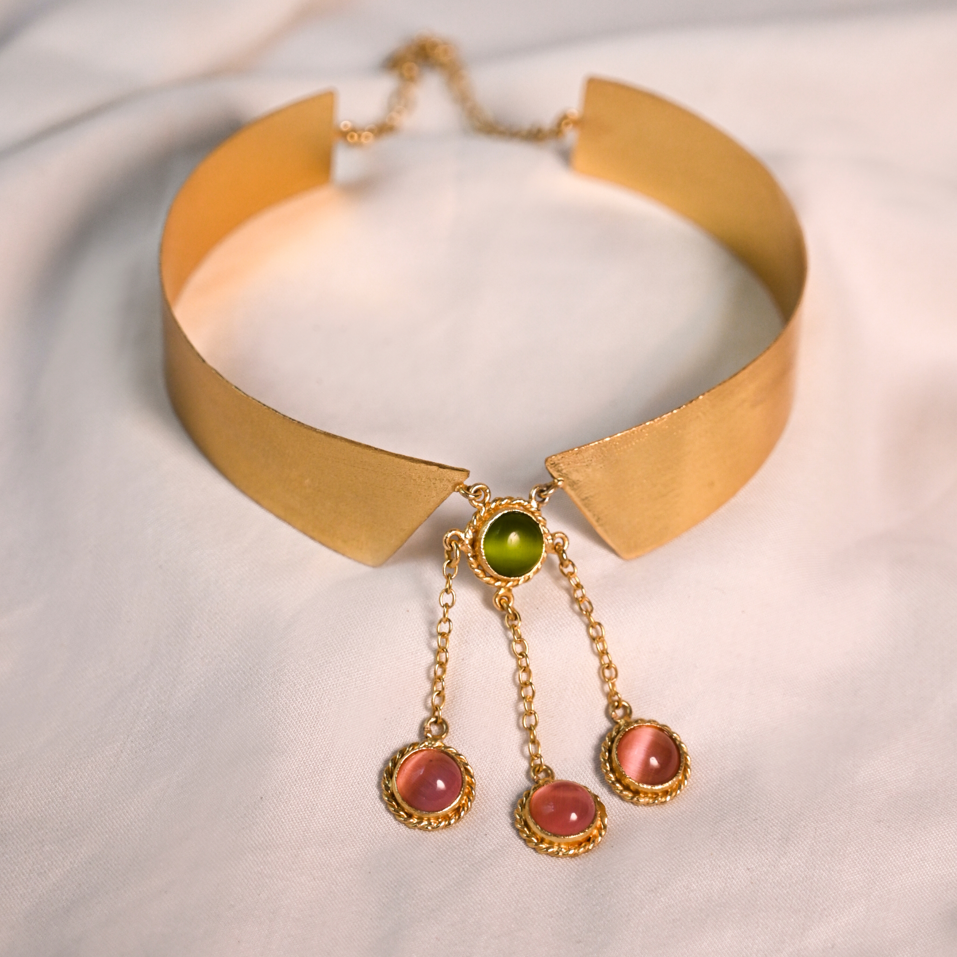 Close-up of an adjustable gold collar necklace with a green center stone and three dangling pink stones.