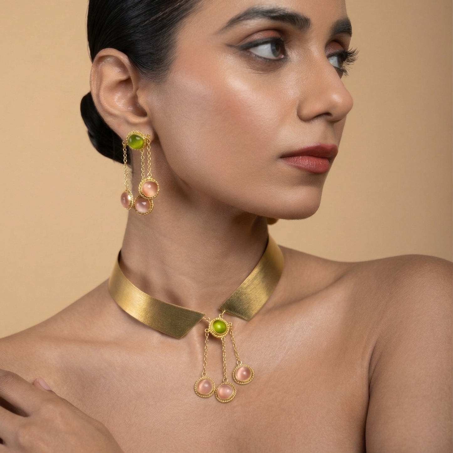 Three-quarter view of a model wearing the gold collar necklace with pink and green stones and coordinating earrings.