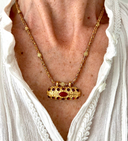 Woman wearing the Mumbai Necklace with its woven cord and gold talisman pendant over a white blouse.
