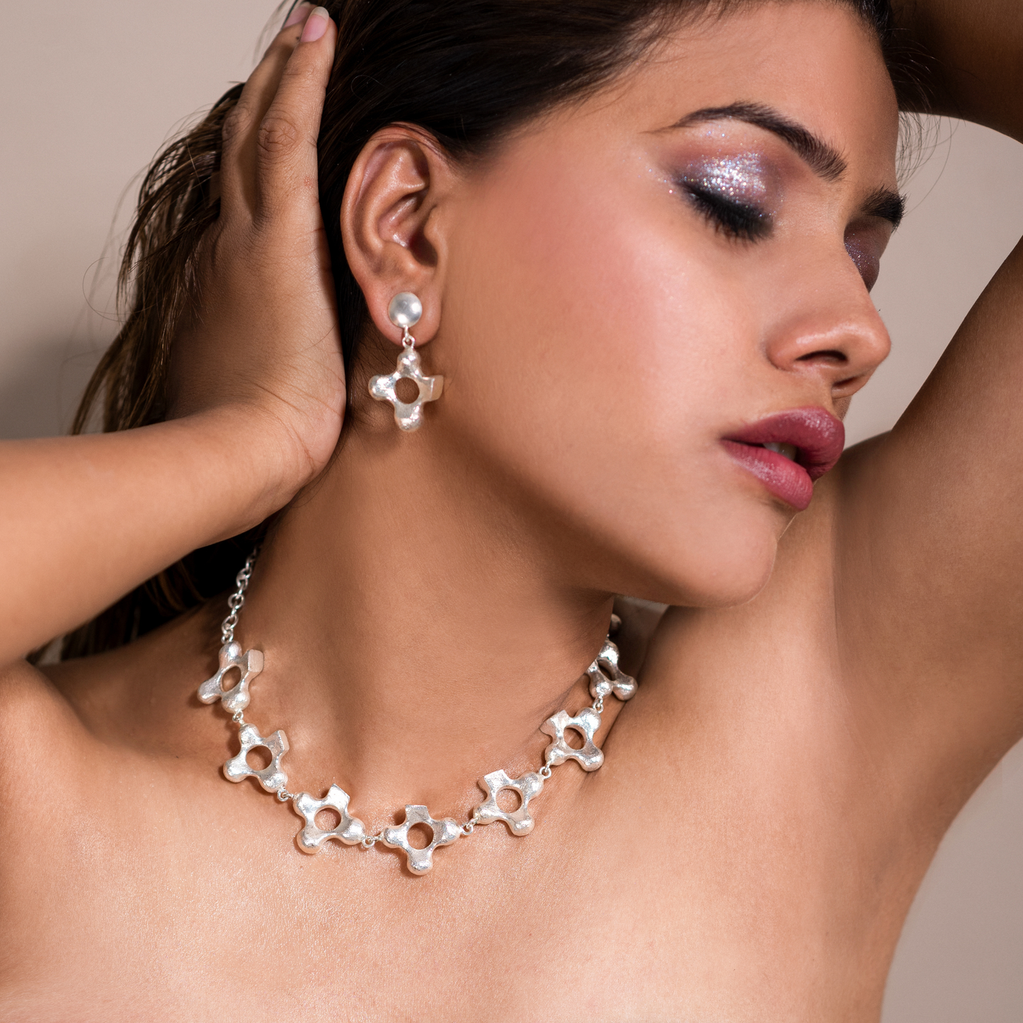 Side portrait of a model wearing the silver-plated sculptural cross necklace and matching earrings.