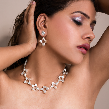 Side portrait of a model wearing the silver-plated sculptural cross necklace and matching earrings.