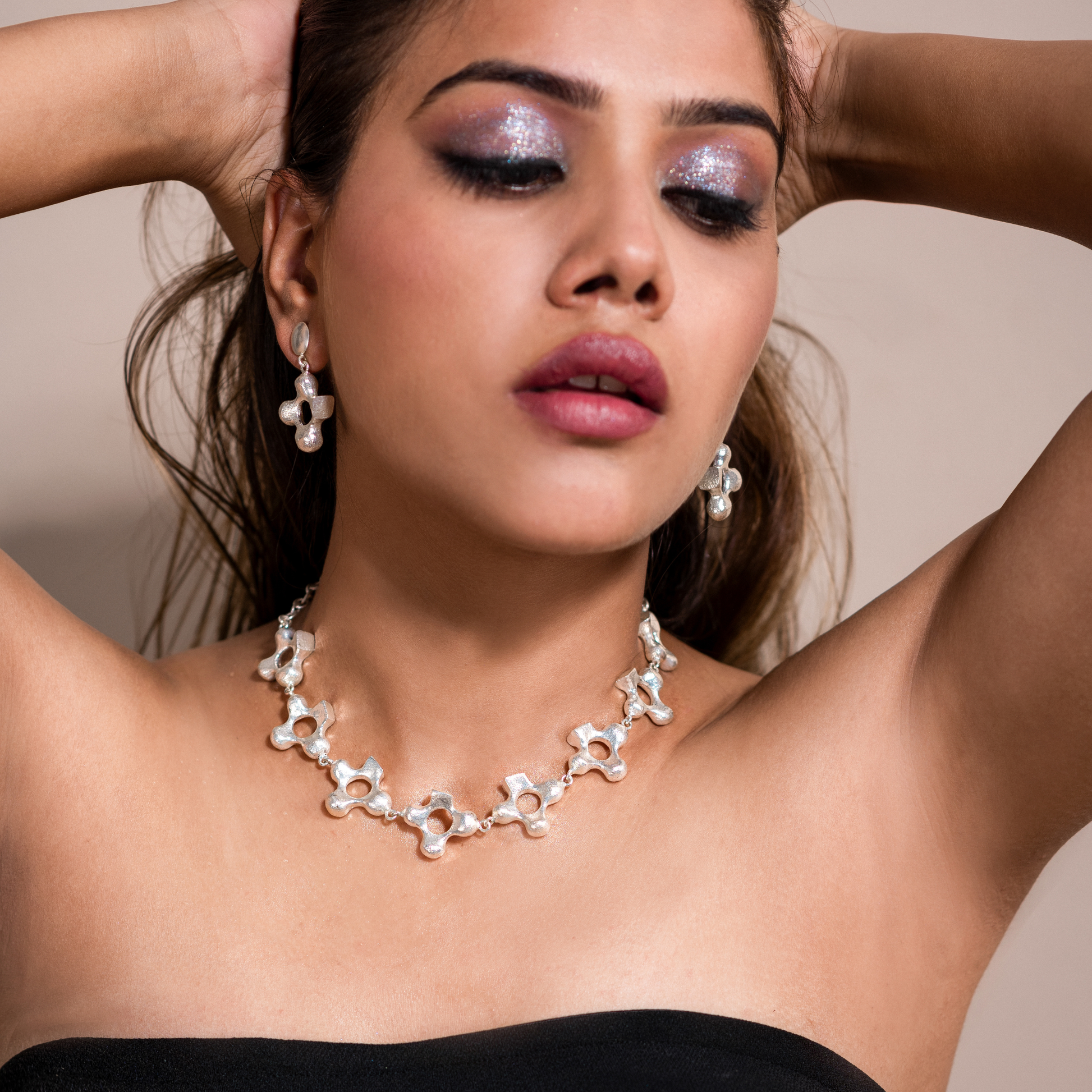 Model posing with raised arms while wearing the silver-plated cross necklace and earrings set.
