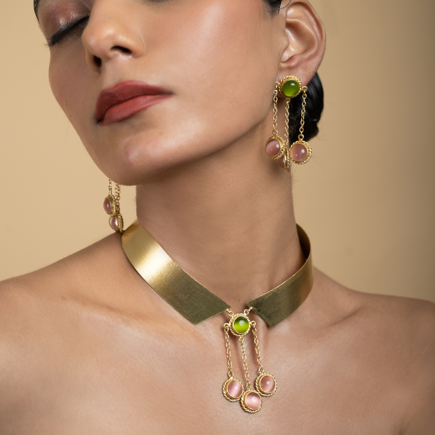 Model wearing sculptural pink and green gemstone earrings with the matching gold collar necklace.