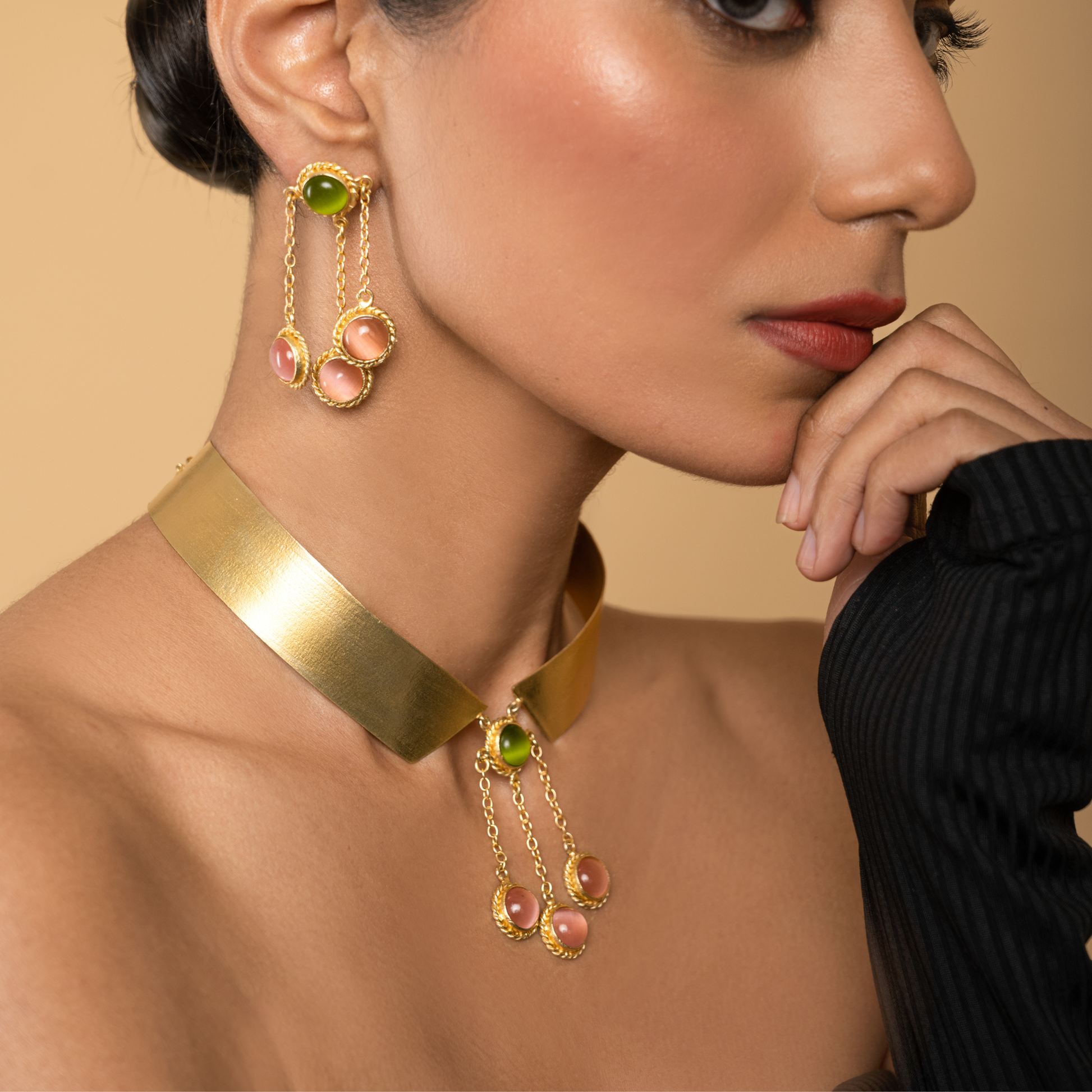Side portrait of a model styling the pink and green gemstone dangle earrings with a gold collar necklace.