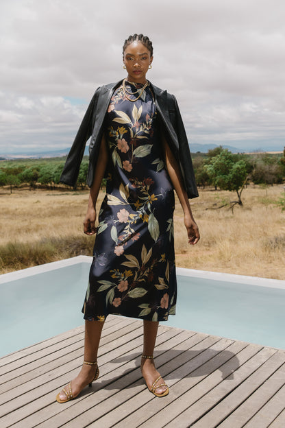 Model wearing the Naf Dress in Sundown Floral styled with a black jacket in an outdoor editorial setting