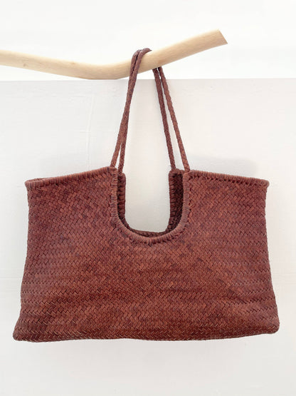 Model carrying the Narmada Brown Bag, a handwoven brown leather tote with an open-top design and spacious silhouette.