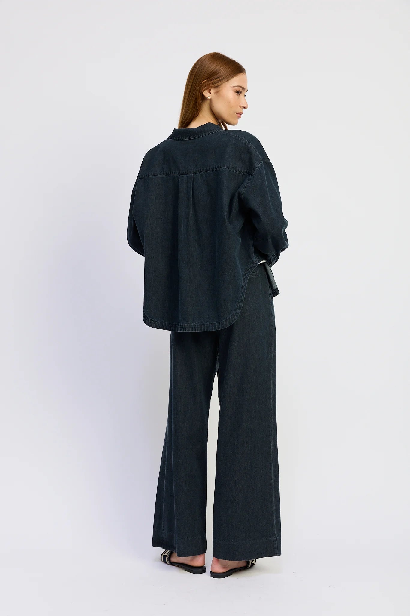 Model wearing the Natalia Top in washed vintage indigo denim, featuring an oversized relaxed fit, dropped shoulders, long sleeves, and a curved hem back view.