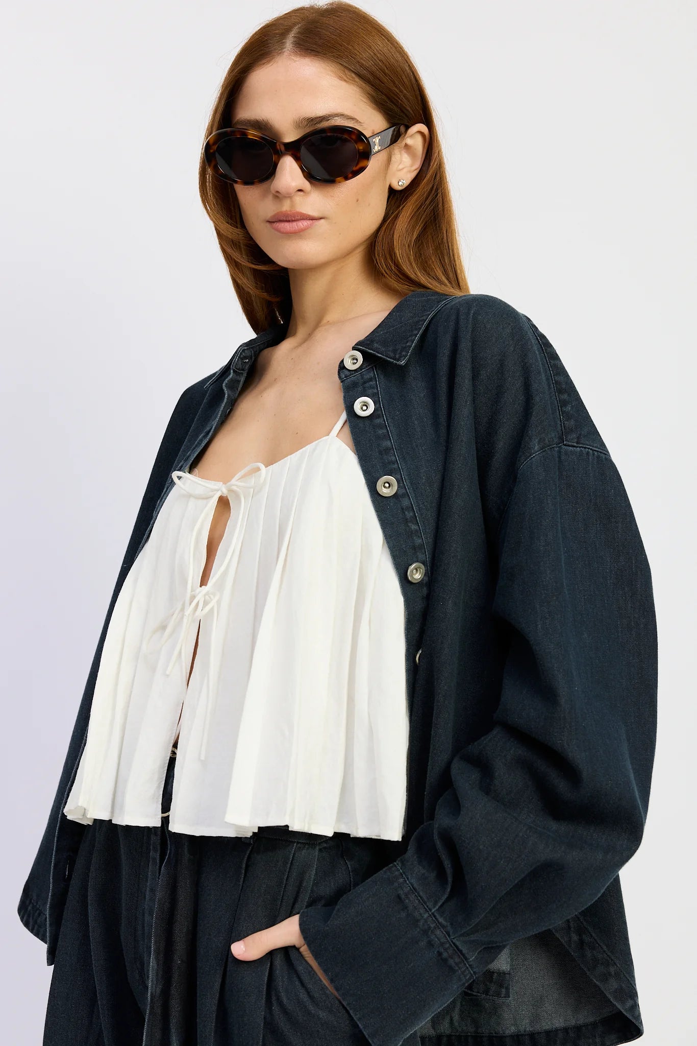 Close-up of the Natalia Top in washed vintage indigo denim styled open over a white tie-front blouse, featuring a relaxed oversized silhouette and button-down front.