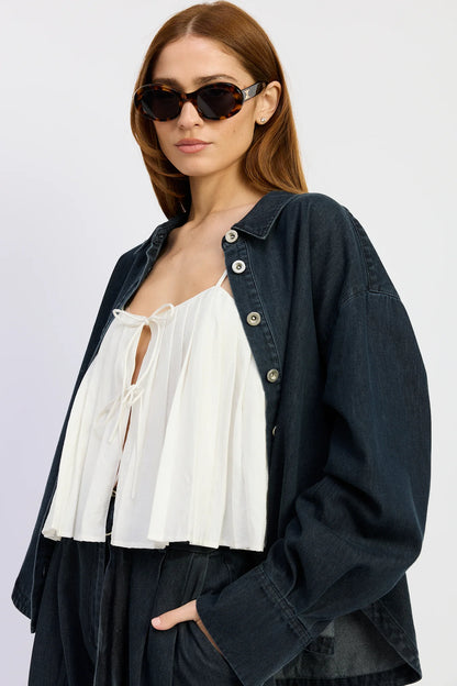 Close-up of the Natalia Top in washed vintage indigo denim styled open over a white tie-front blouse, featuring a relaxed oversized silhouette and button-down front.