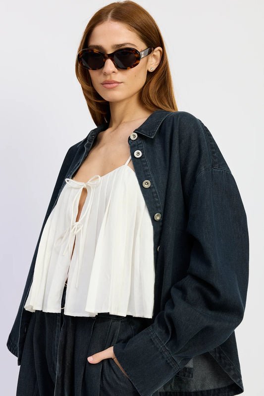 Close-up of the Natalia Top in washed vintage indigo denim styled open over a white tie-front blouse, featuring a relaxed oversized silhouette and button-down front.