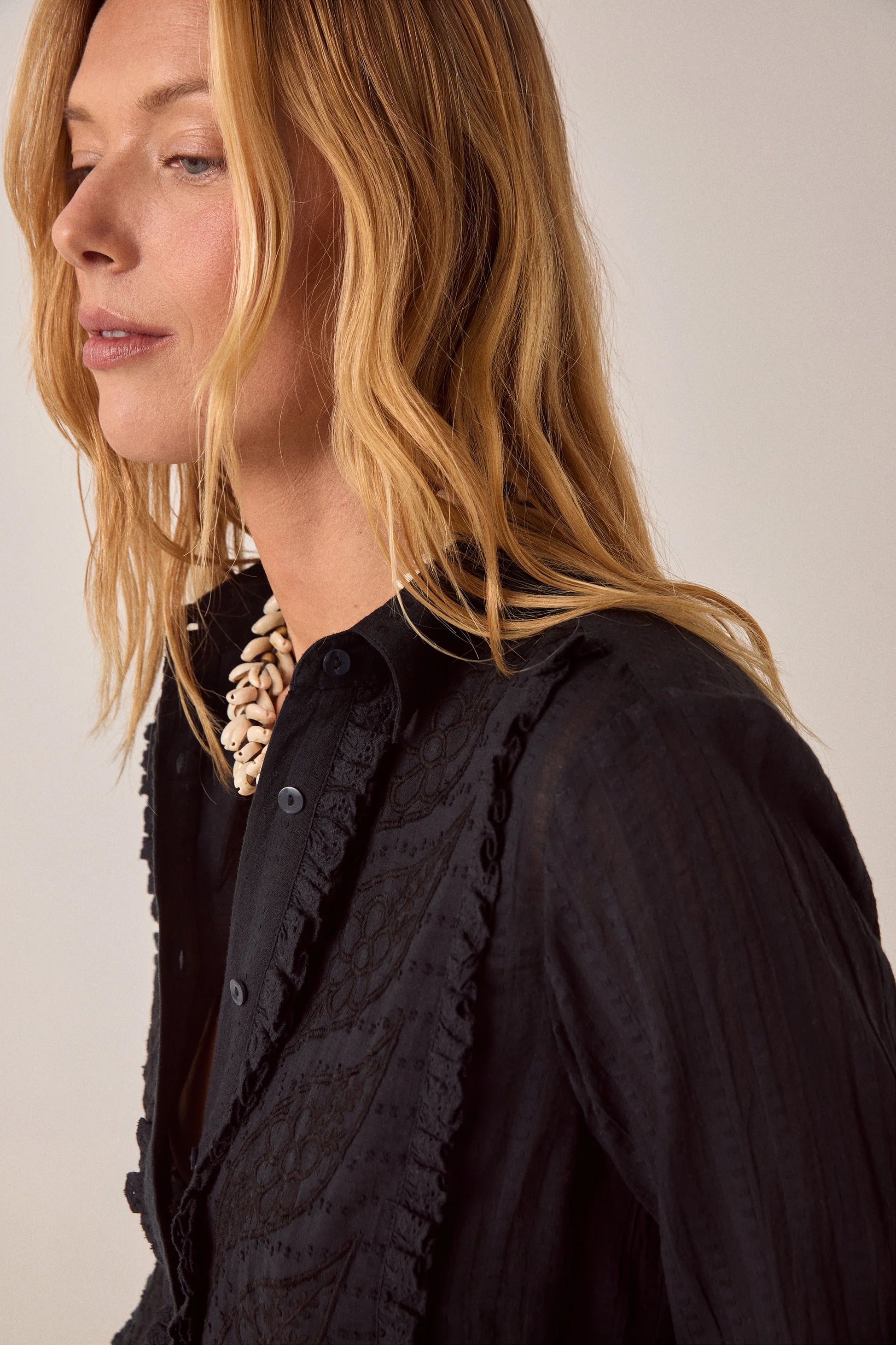 Side close-up of the Night Fever Javiera Blouse in Onyx showcasing tonal floral embroidery, soft ruffle trim, and lightweight textured cotton.