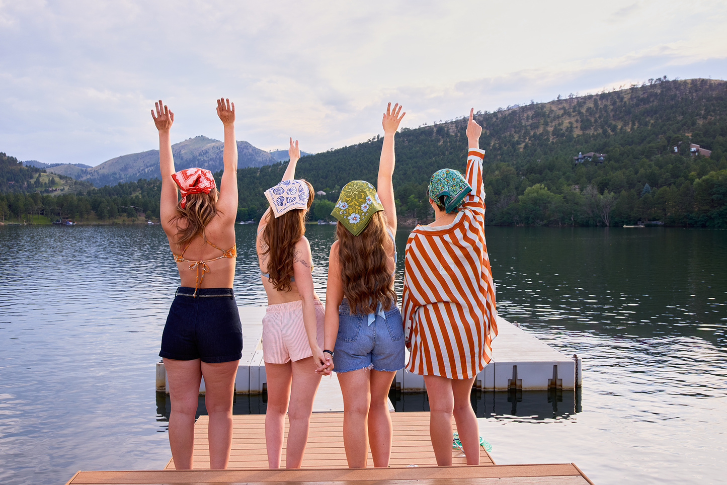 Group wearing colorful bandanas on a lakeside dock, including the Clara bandana in olive green with periwinkle floral details.