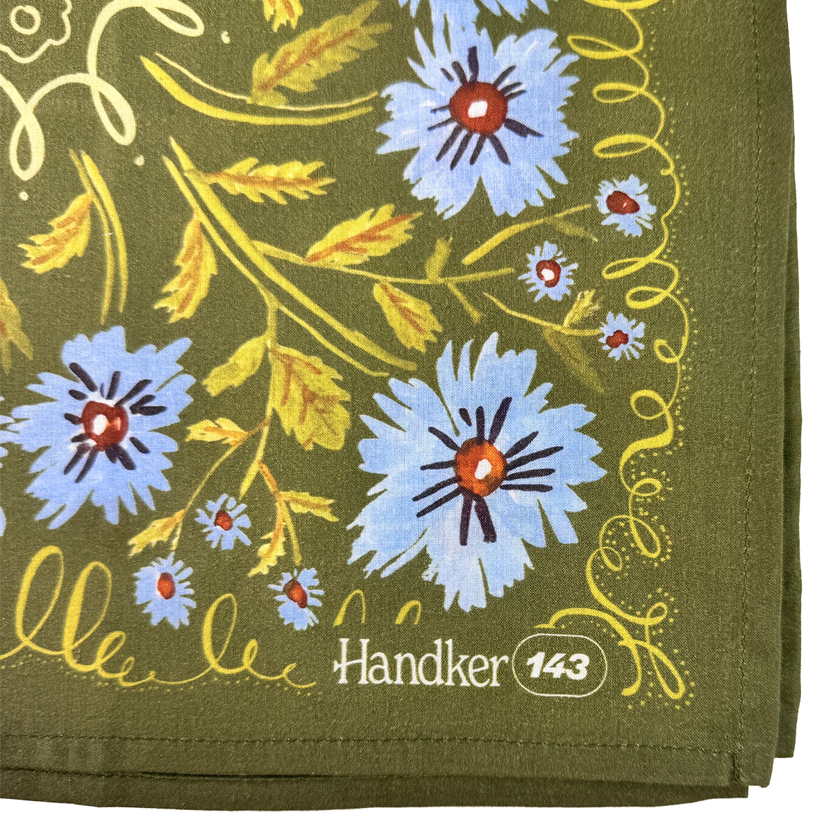 Close-up of the Clara bandana showing periwinkle flowers, olive green cotton fabric, yellow botanical details, and stitched edges.