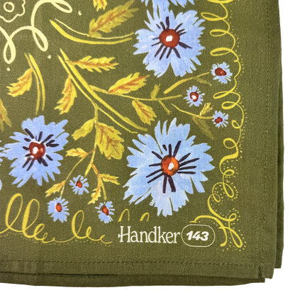 Close-up of the Clara bandana showing periwinkle flowers, olive green cotton fabric, yellow botanical details, and stitched edges.
