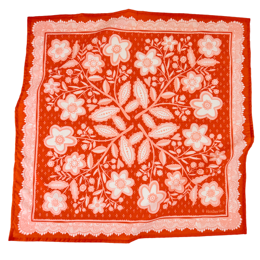 Red-orange and pink Lacey Bandana laid flat, featuring an intricate floral pattern and decorative border.