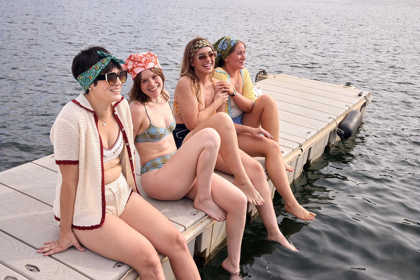 Group of women sitting together by the water wearing colorful bandanas in their hair.