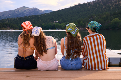 Group of friends sitting beside a mountain lake wearing colorful bandanas as headscarves.