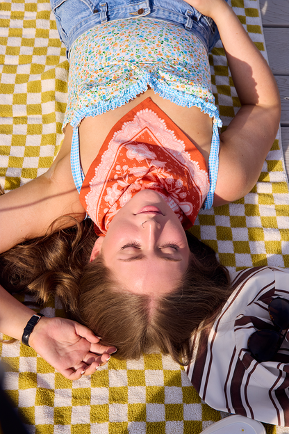 Woman lying on a patterned blanket with the Lacey Bandana tied around her neck.