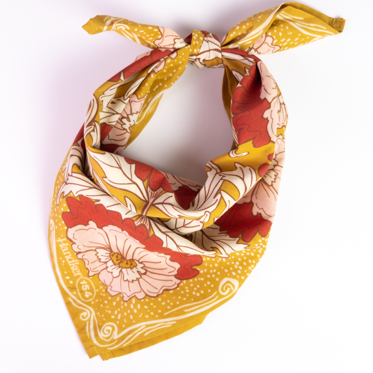 Ruthie Bandana loosely knotted to showcase its ochre gold, pink, brown, and cream floral pattern.