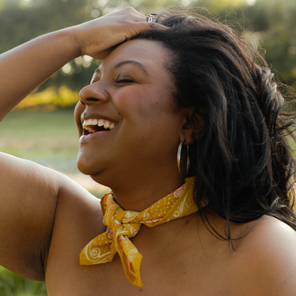 Model wearing the Ruthie Bandana tied around the neck in its ochre gold and pink floral print.