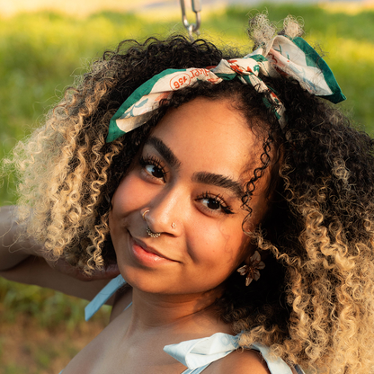 Woman wearing the No. 156 Willa Bandana tied around her curly hair in an outdoor setting.