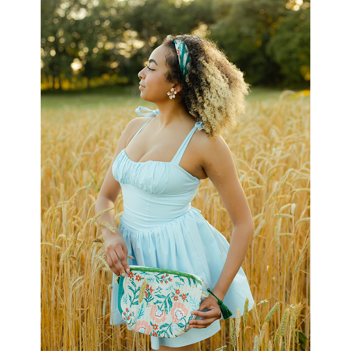 Woman styling the No. 156 Willa Bandana at her waist with a light blue dress in a field.