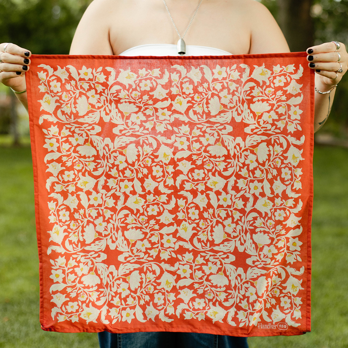 Woman holding the No. 159 Delphine Bandana open to show its full botanical design.