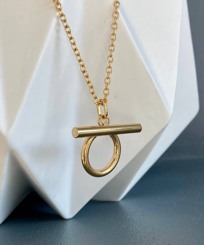 Detail view of the gold Omega Necklace and its sculptural Omega-shaped pendant on a white display.