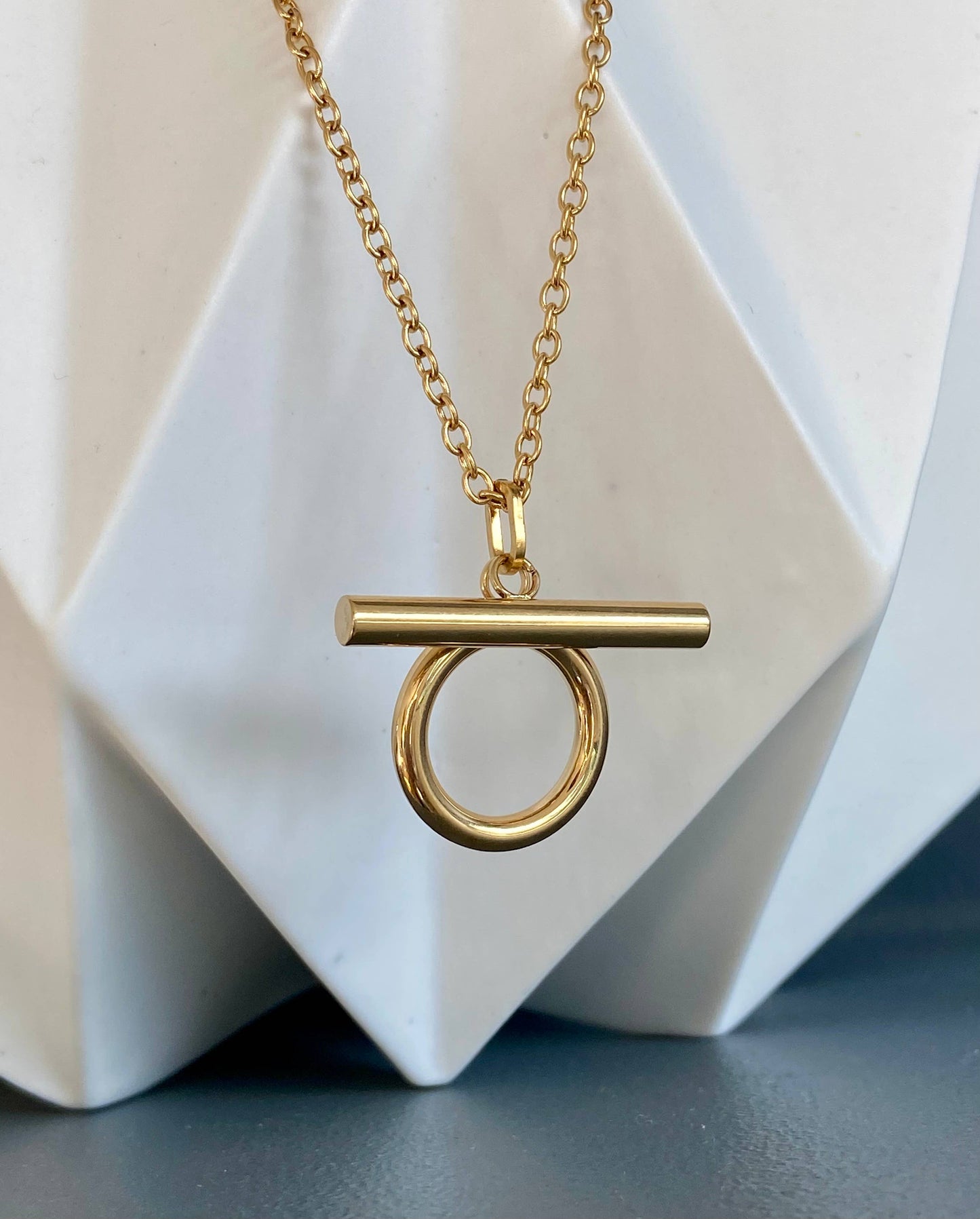 Gold Omega Necklace displayed on a white sculptural stand, showing the chain and pendant design.