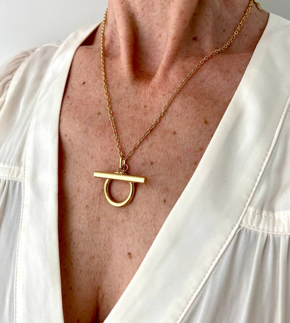Close-up of the gold Omega Necklace worn with a white V-neck blouse.