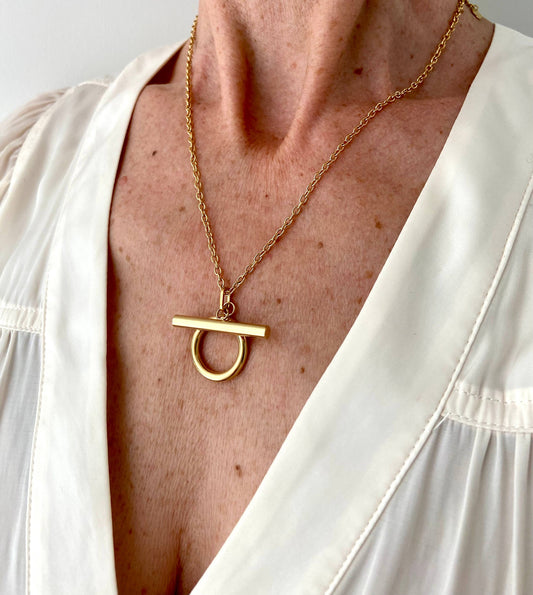 Close-up of the gold Omega Necklace worn with a white V-neck blouse.