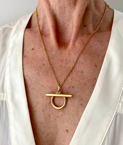 Front view of the gold Omega Necklace worn at the neckline of a white blouse.