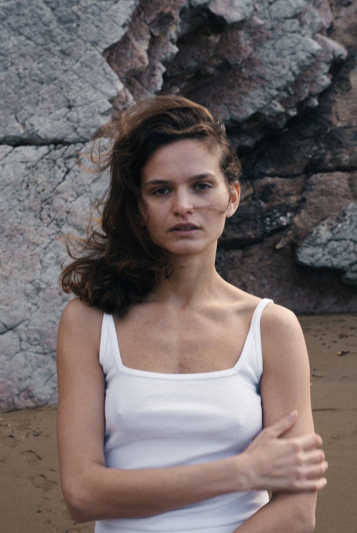 Model wearing the Organic Square Cami in white with relaxed white pants on a rocky beach.