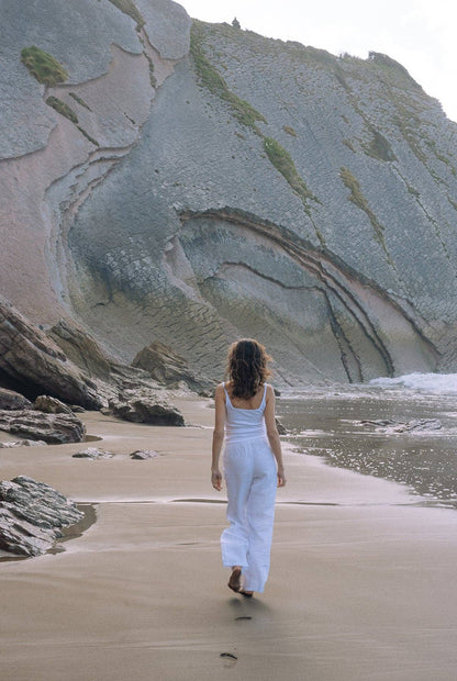 Organic Square Cami in white styled with white pants while walking along a rocky shoreline.