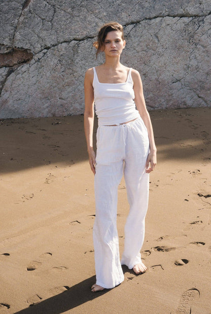 Full outfit view of the Organic Square Cami in white paired with relaxed white pants on a sandy beach.