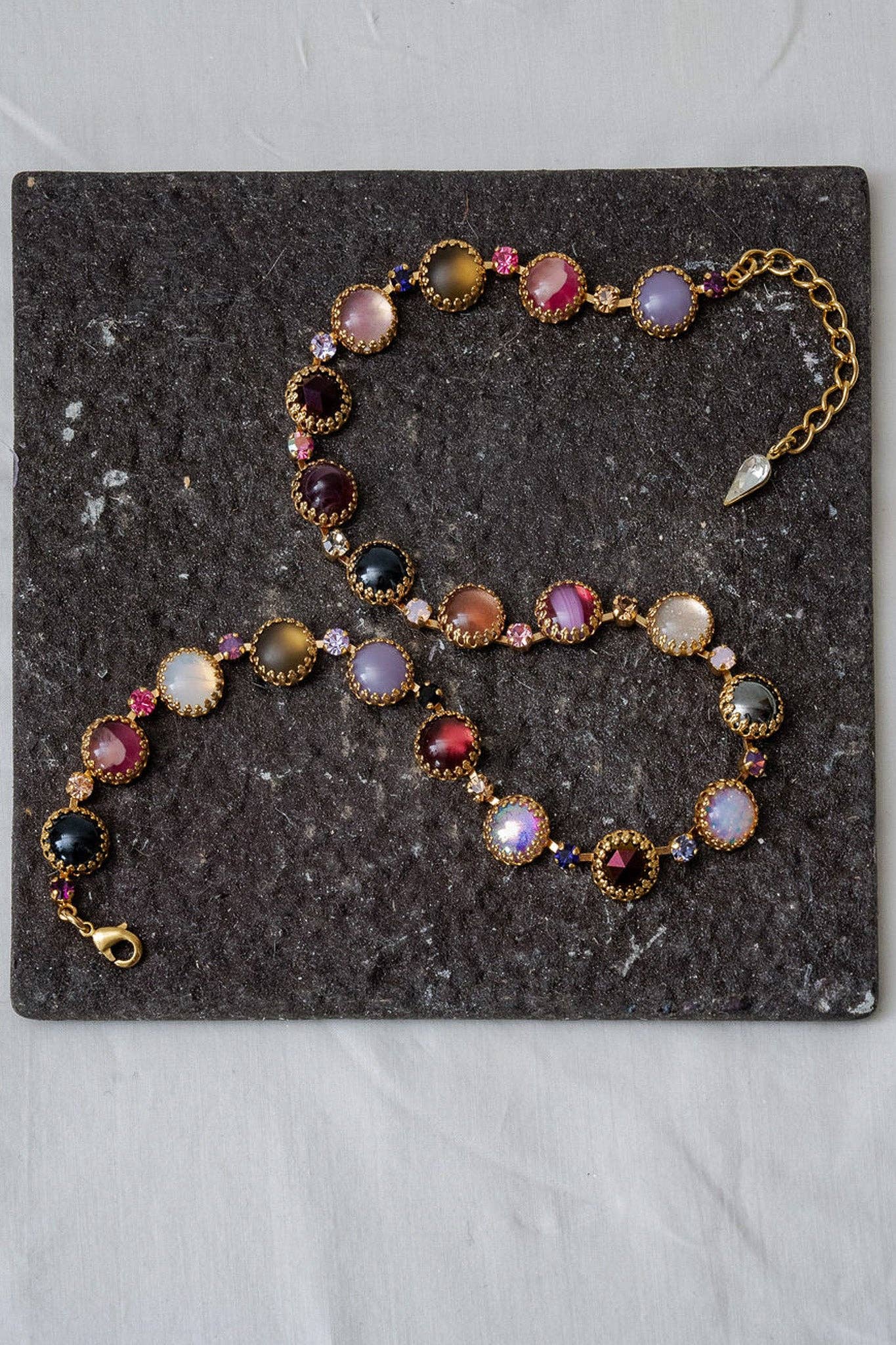 Paint Pot Layering Choker in Punk Rocks Gold displayed on a dark stone surface with multicolor round stones and gold-plated settings.
