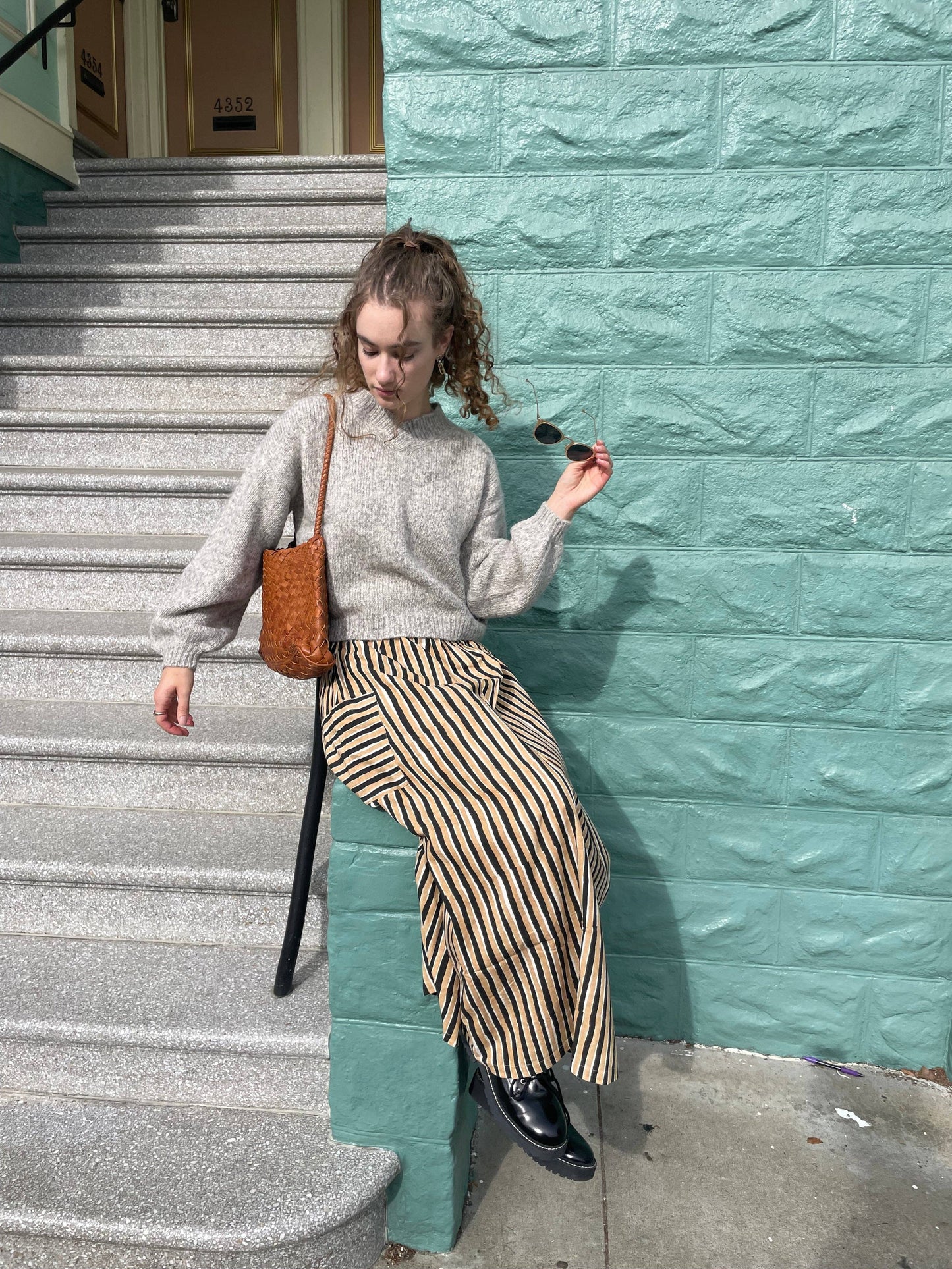 Full-length view of a model carrying the Palar Tan Bag beside a mint green wall